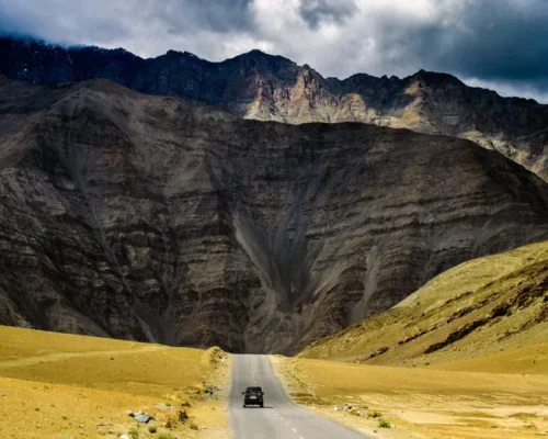 Black SUV drives on a winding road through a barren mountain landscape under a dramatic sky.