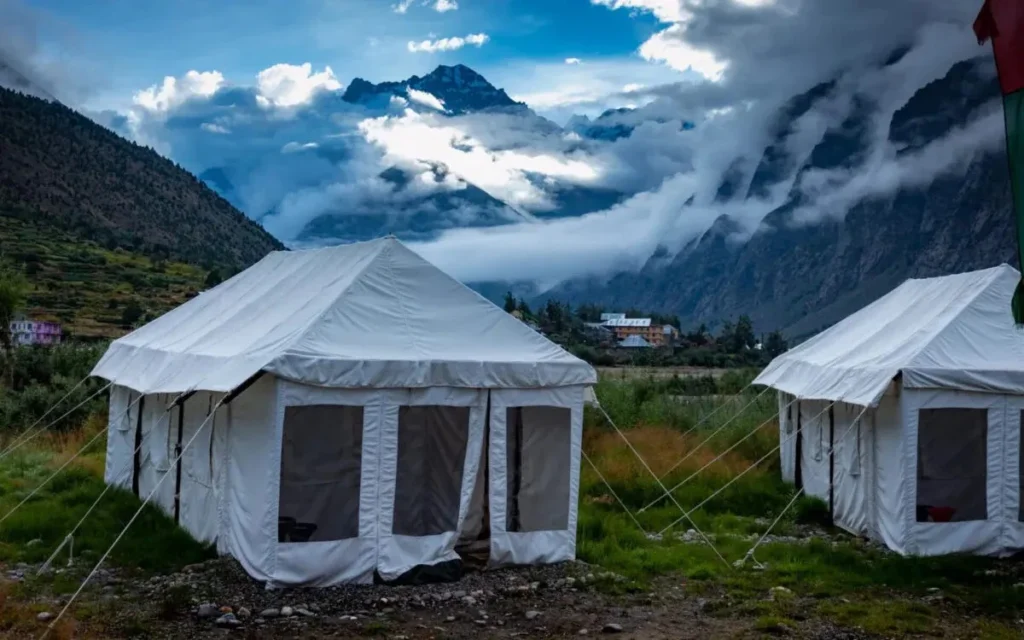White canvas tents set up in a valley with dramatic cloudy mountains in the background.