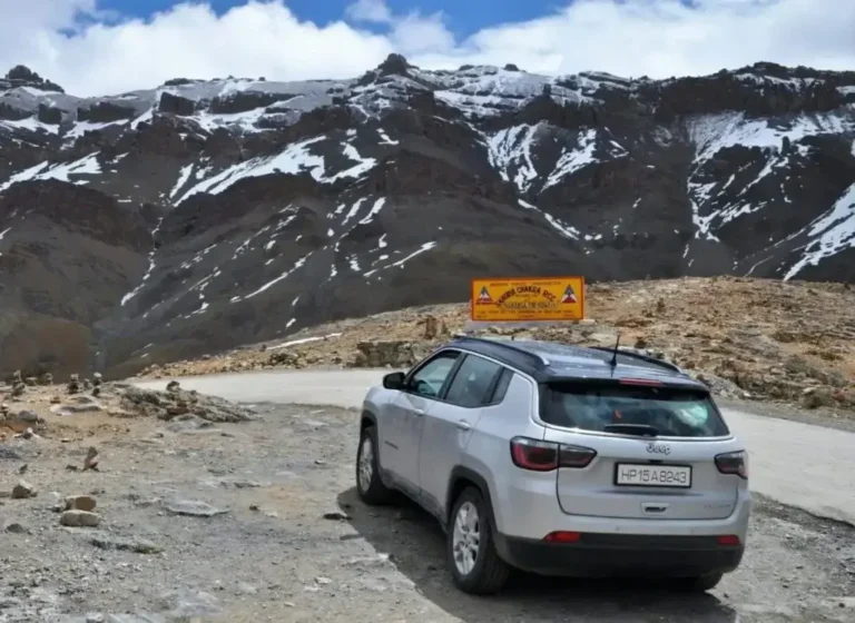 Grey parked on a gravelly mountain road with rocky cliffs in the background.